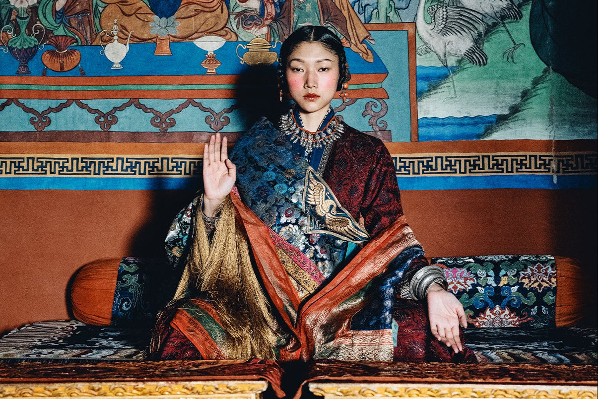 Woman in traditional attire sitting on a decorated chair with a colorful mural in the background
